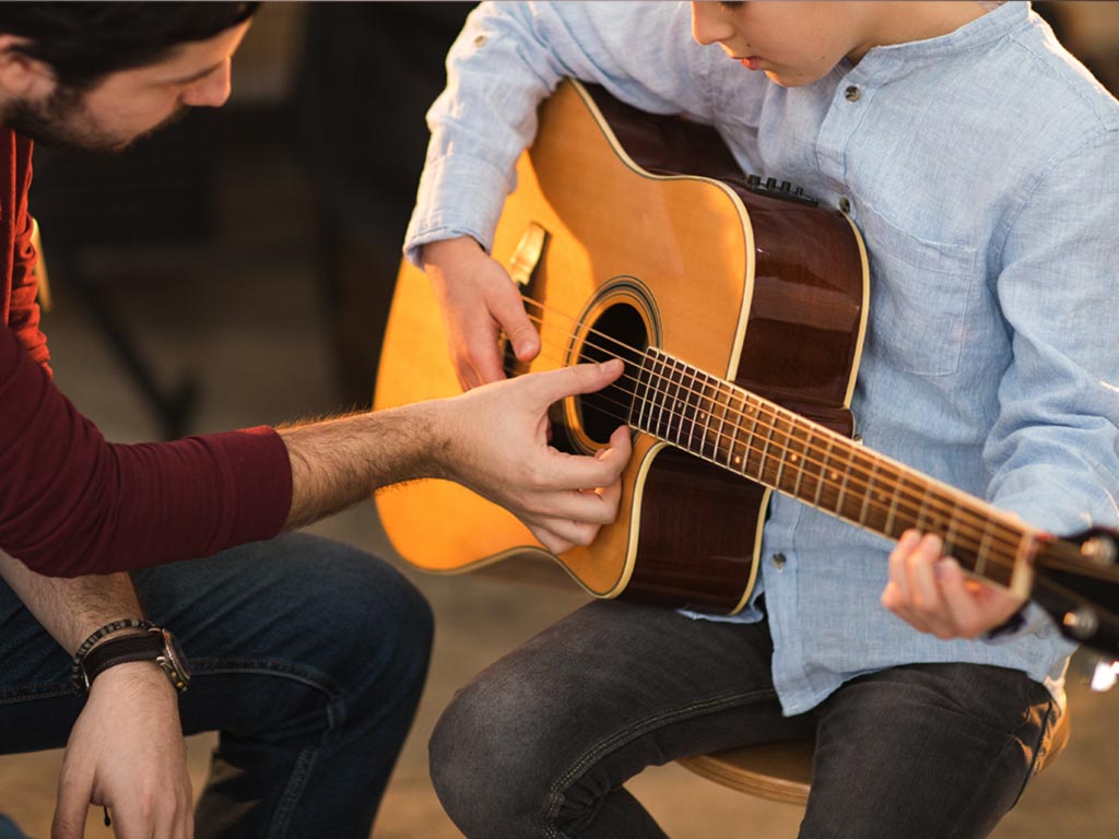 Child learning guitar with teacher